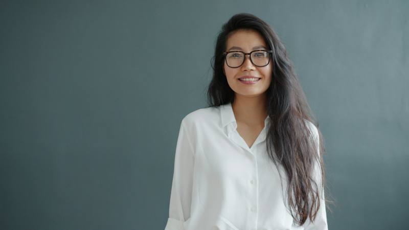 A woman with glasses smiles against a gray background