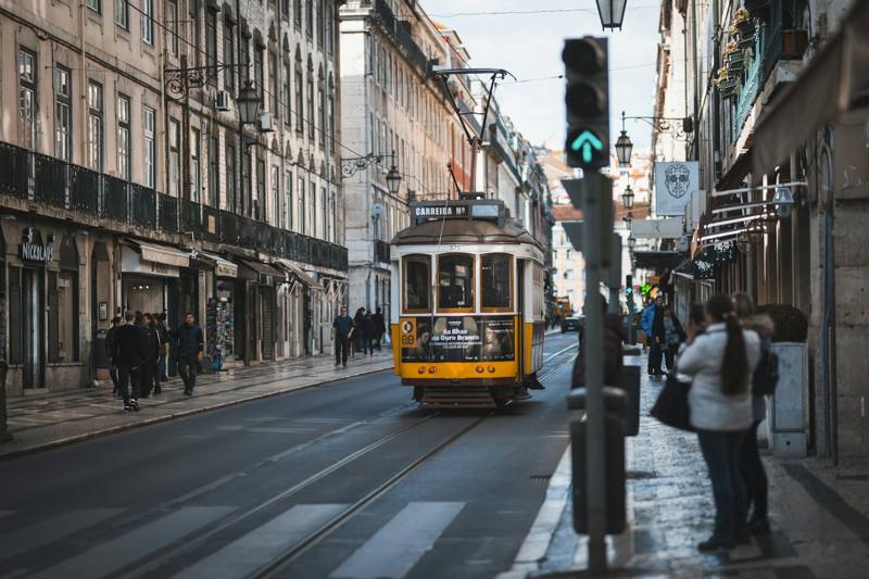 People standing on pathway in front of white and yellow tram on road during daytime